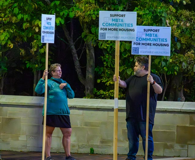 Two people holding signs in support of the MBTA Communities proposal in front of Arlington Town Hall.