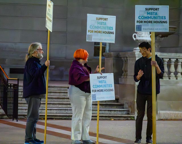 Three people holding signs in support of the MBTA Communities proposal demonstrating outside Arlington Town Hall