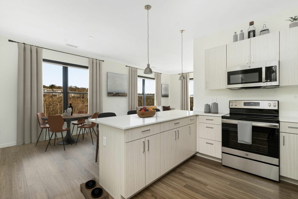 Interior of an apartment at The Artemis at Arlington Heights. A white kitchen with shaker style cabinets opens to a dining area with views over Arlington.