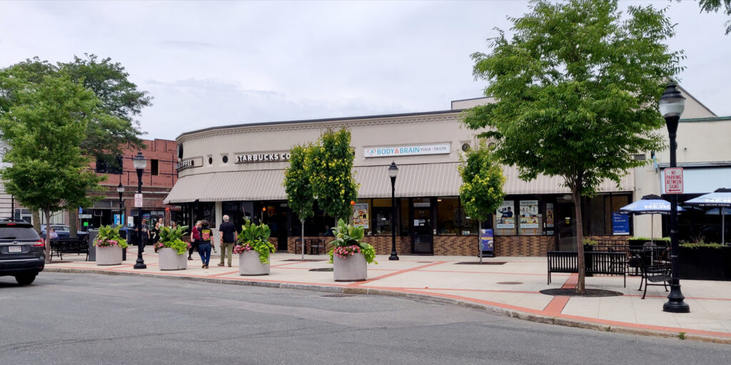 No parking zone in front of Broadway plaza.  The plaza contains a number of trees and planters, and there are several storefronts behind the plaza.